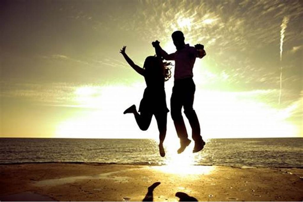 a man and woman jumping on a beach